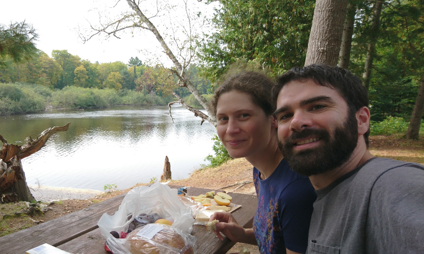 Picture of my wife and I having a picnice of bread and butter, apples and cheese on the bank of the Tahquamenon River.